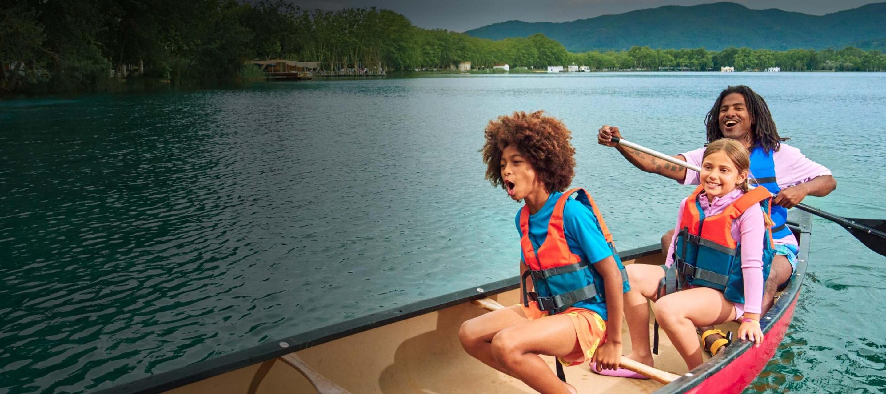 Deux enfants et un adulte rient en traversant un lac en canoë. 