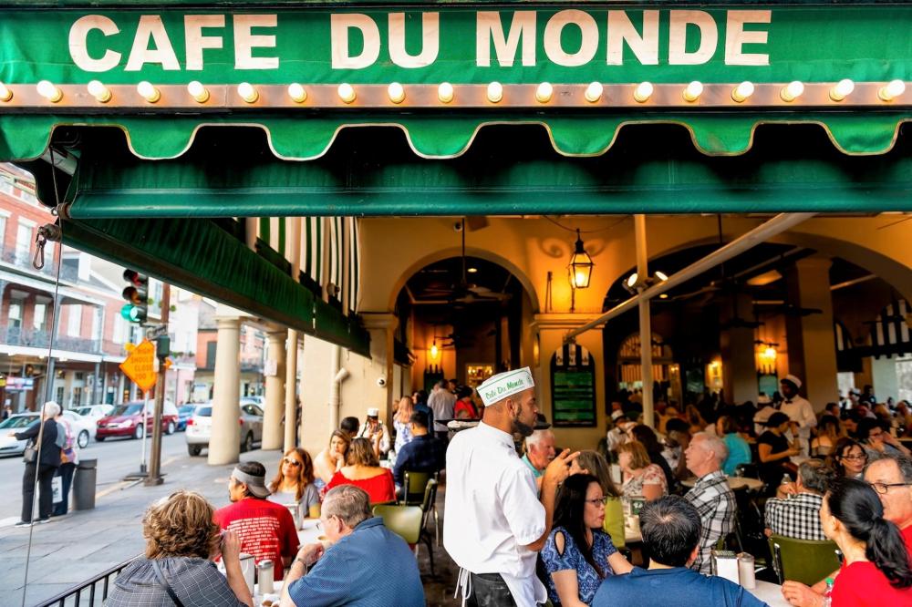 Exterior view of Café Du Monde in New Orleans, featuring its iconic green and white awning and outdoor seating
