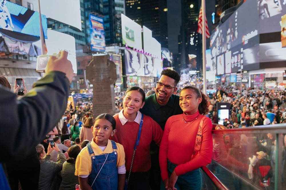 A family poses for a photo in Times Square, surrounded by bright lights and bustling crowds