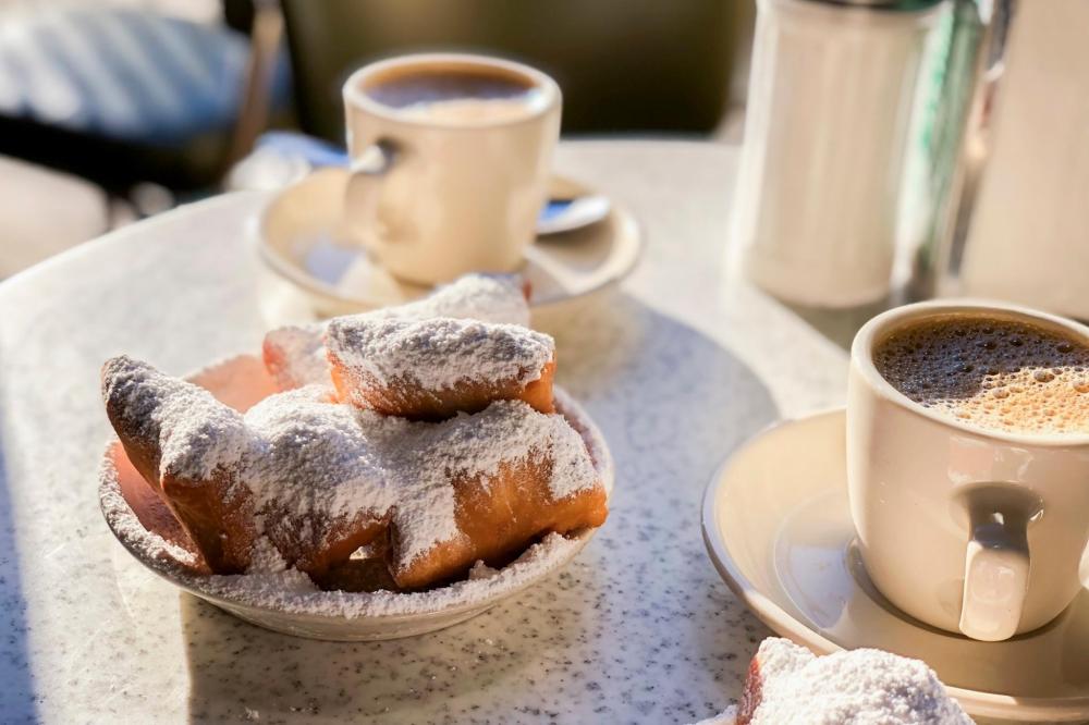 A table featuring a plate of beignets dusted with powdered sugar alongside a steaming cup of coffee