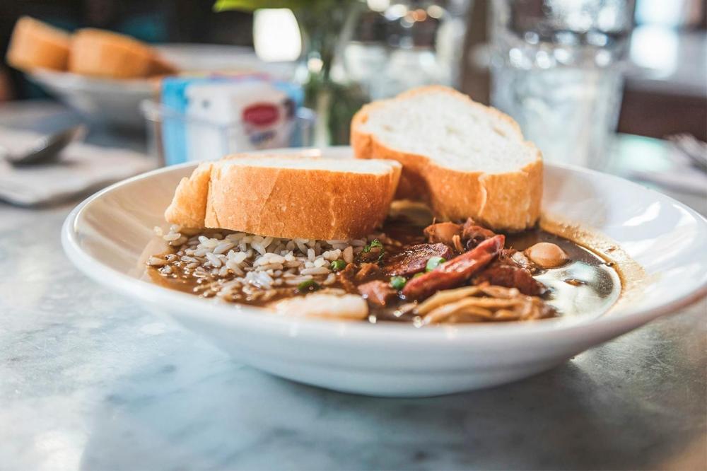 A bowl of gumbo, a signature New Orleans dish, filled with shrimp, sausage, and vegetables in a rich, flavourful broth