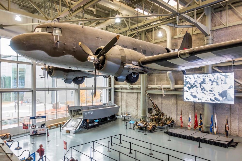 A large airplane suspended in The National WWII Museum, surrounded by a visitors admiring the exhibit