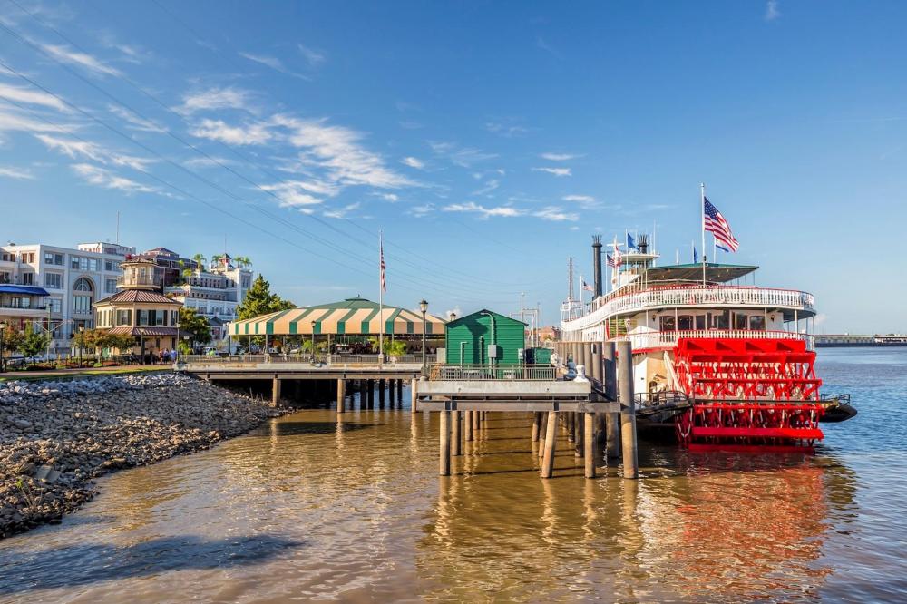 A steamboat docked at a pier in New Orleans, surrounded by water and city scenery