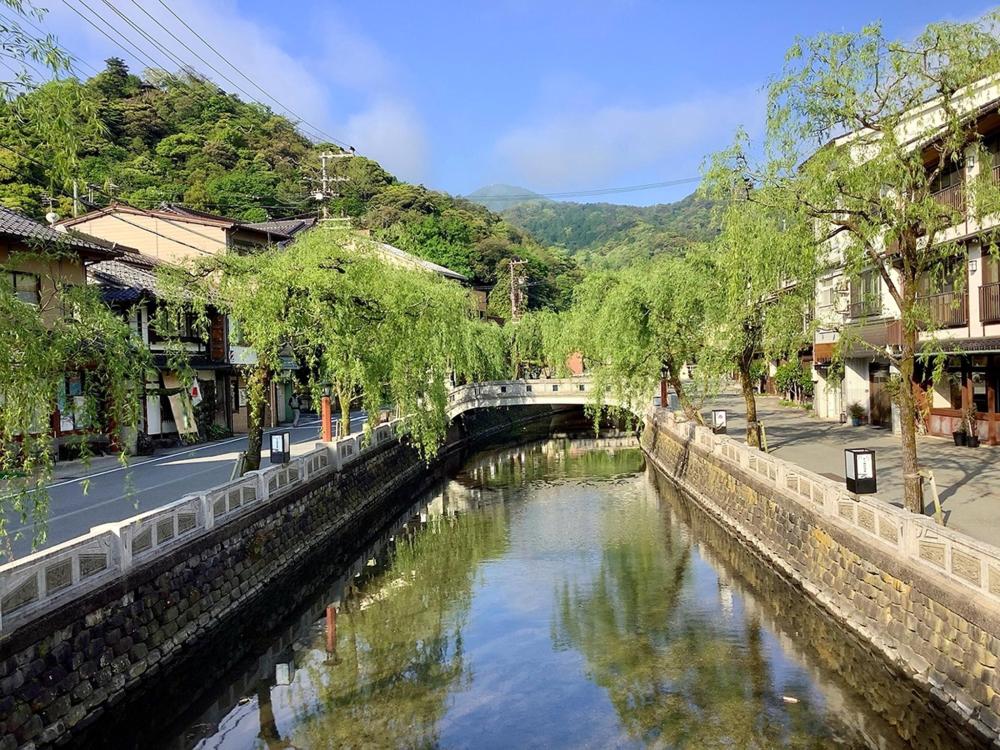 A canal in Kinosaki, Toyooka, surrounded by quaint buildings and trees, reflecting the town's charm.