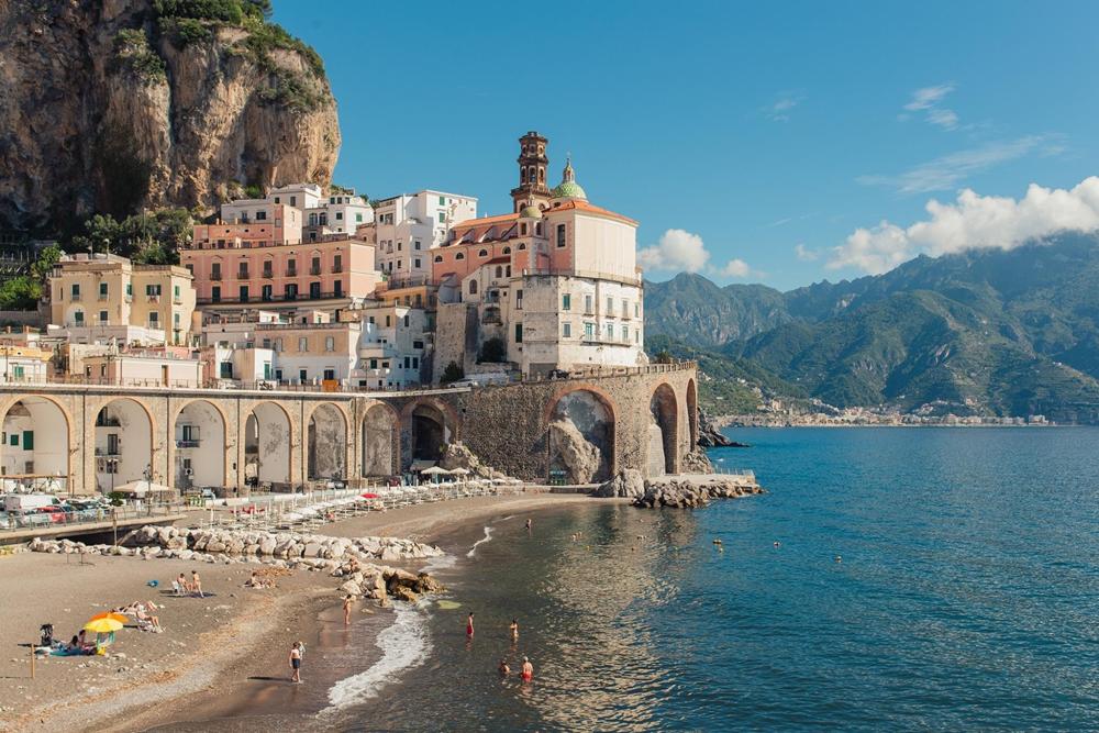 A scenic view of the Amalfi Coast featuring a beach, rocky cliffs, and charming buildings along the shoreline