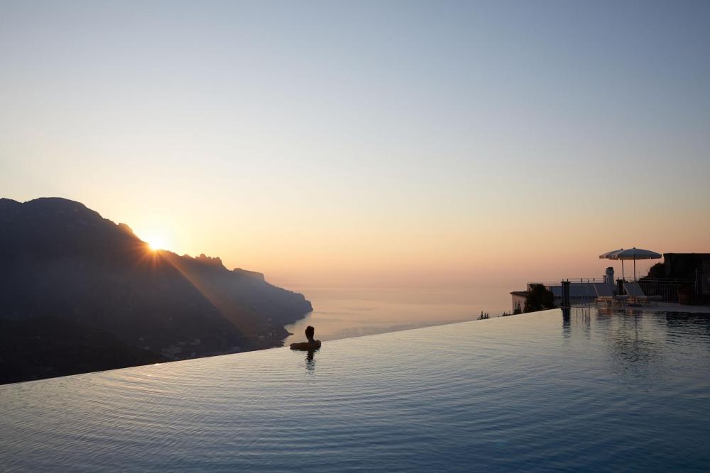 A sunset over the ocean, viewed from an infinity pool at Belmond Hotel Caruso, Italy, casting warm hues across the sky