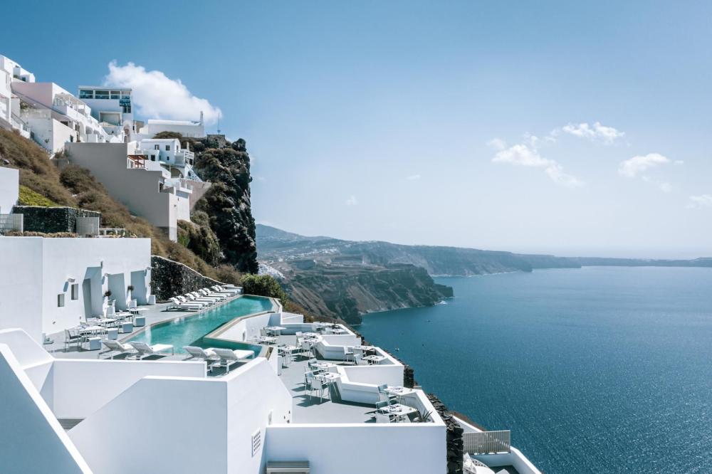 A stunning view of the sea and white buildings on a cliff, featuring the infinity pool at Grace Hotel Santorini, Greece
