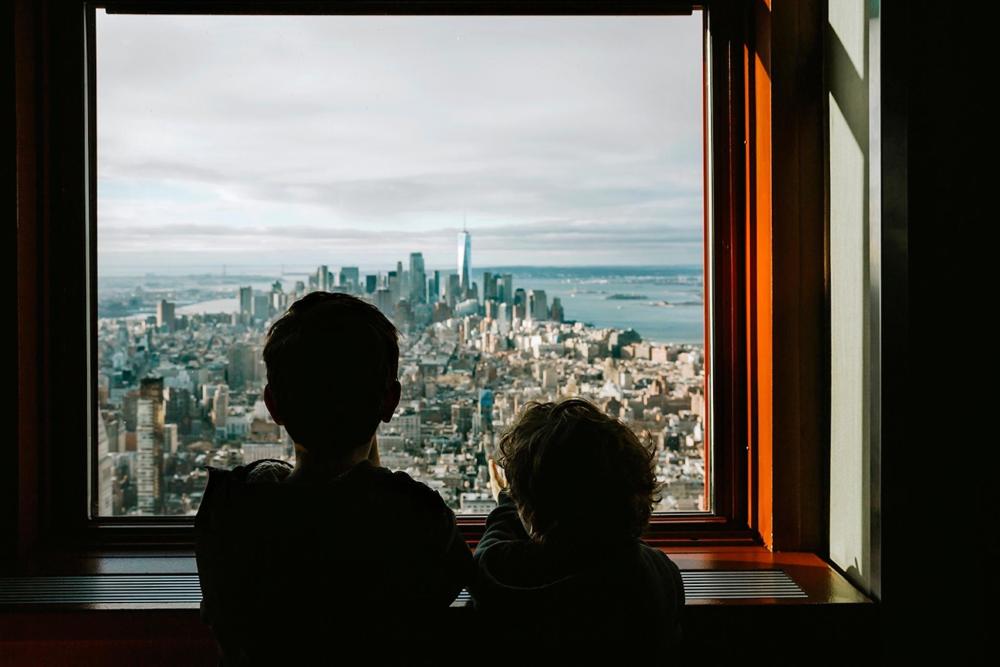 Two children gaze out of a window onto a bustling cityscape