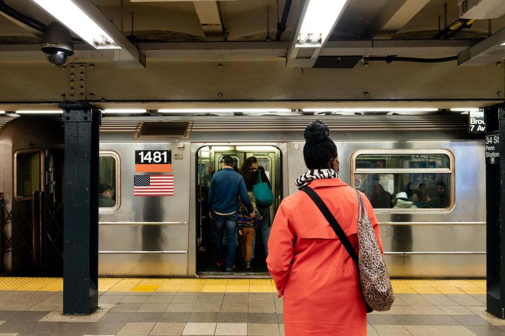 A woman stands confidently in front of a subway train, ready for her journey ahead
