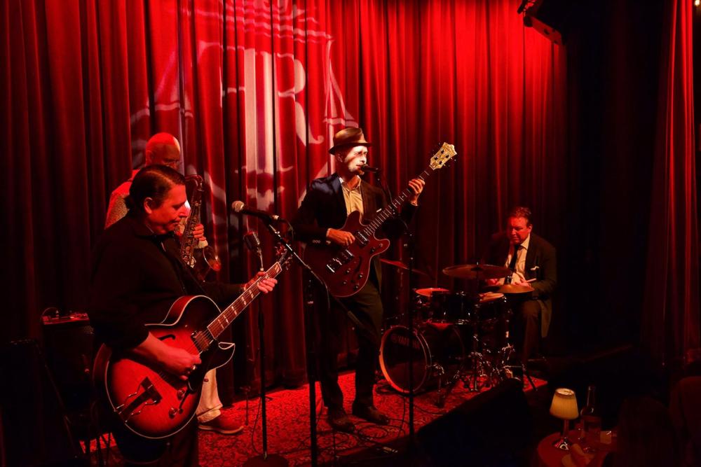 A jazz band performs on stage, surrounded by vibrant red lighting, creating a lively atmosphere