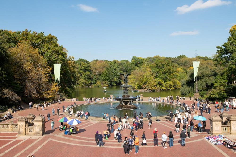A group of people stroll around a fountain in Central Park, enjoying the scenery and atmosphere