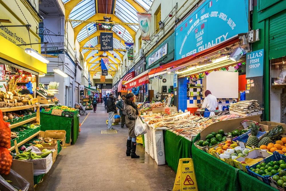 Brixton Market is bustling with shoppers exploring vibrant stalls filled with fresh fruits and vegetables