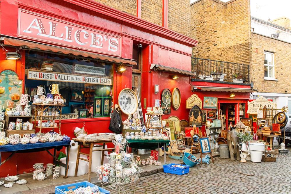 A red shop called Alice's on Portobello Road adorned with various antiques displayed along its side