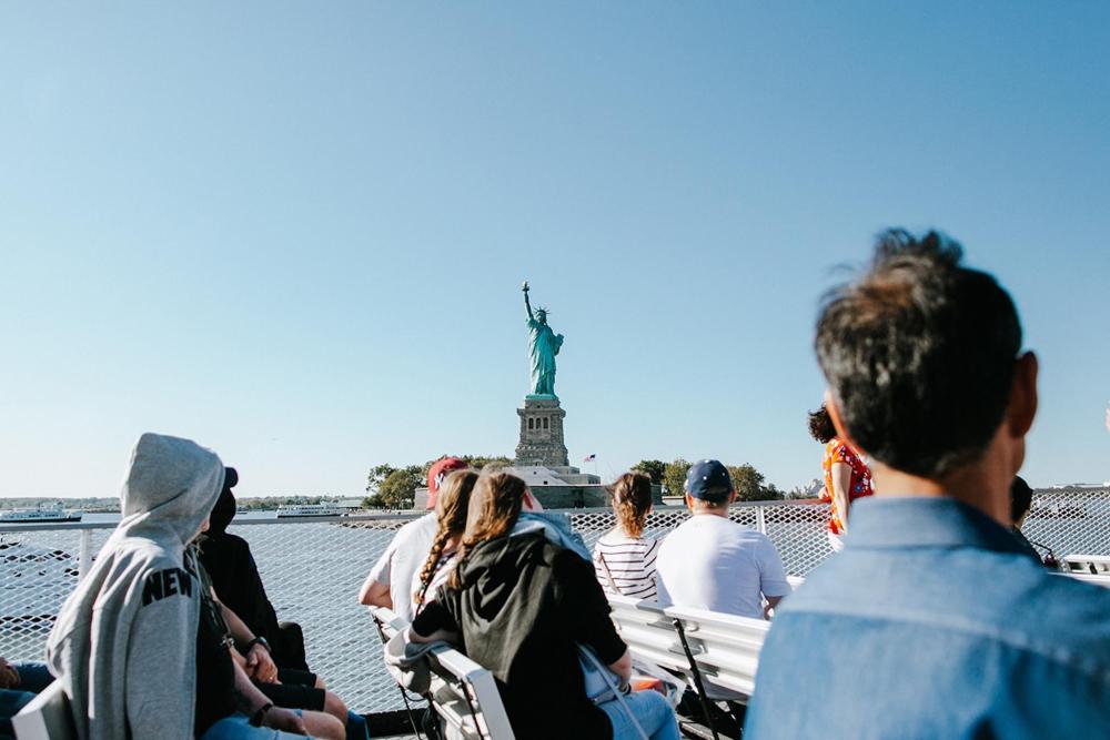 A group of people on a boat gazing at the Statue of Liberty against a clear blue sky.