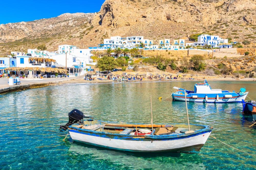 Barchette ormeggiate nelle acque limpide di una spiaggia a Rodi, davanti a un placido paesaggio costiero