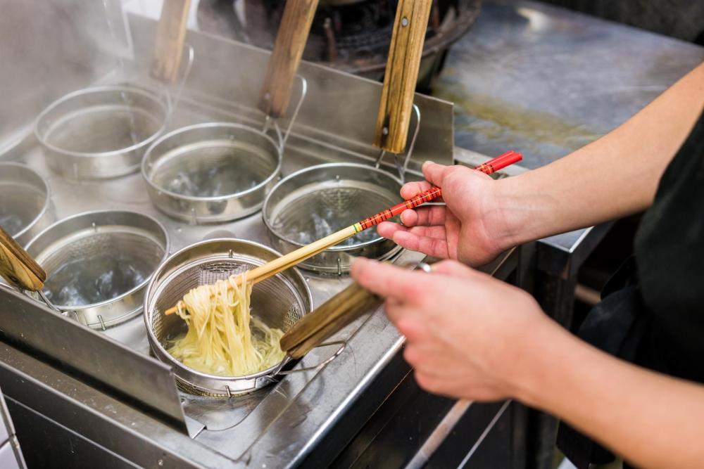 A person stirs ramen noodles in a pot, showcasing the cooking process and steam rising from the dish