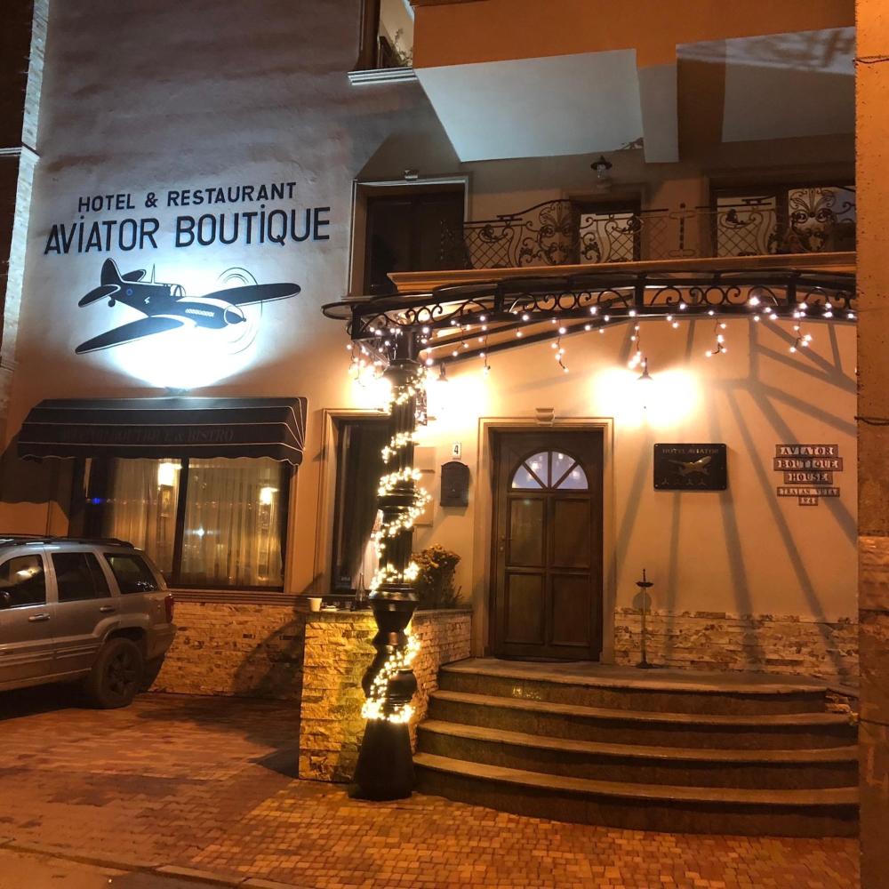 The outside of Hotel Aviator Boutique in Otopeni, Romania is depicted. The logo is on the outside of the building and there are some fairy lights around the entrance