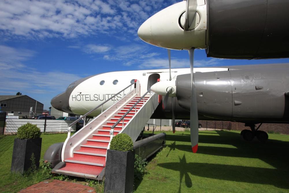 The Vliegtuigsuite Teuge is depicted, with red plane stairs leading into the cabin. The plane hotel is located on some grass