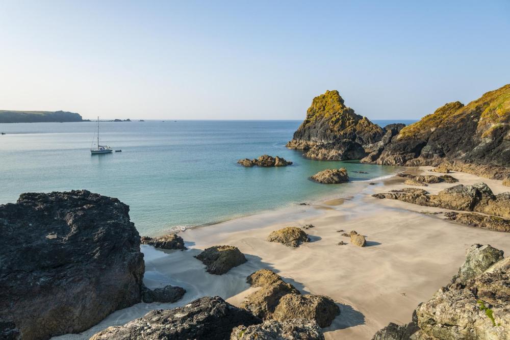 An impressive landscape is depicted, with golden sands and jagged cliffs. A boat can also be seen in the body of water at Kynance Cove