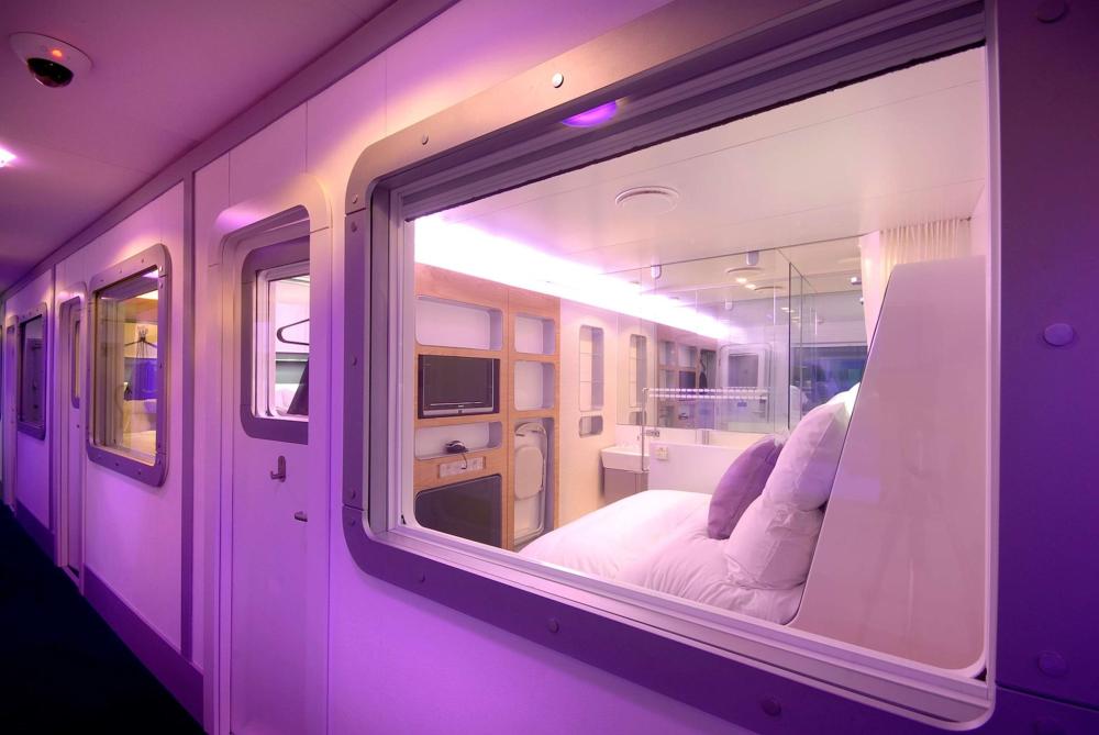 A purple light illuminates the interiors of capsule hotel rooms, casting a vibrant glow at YOTELAIR, London Gatwick Airport.