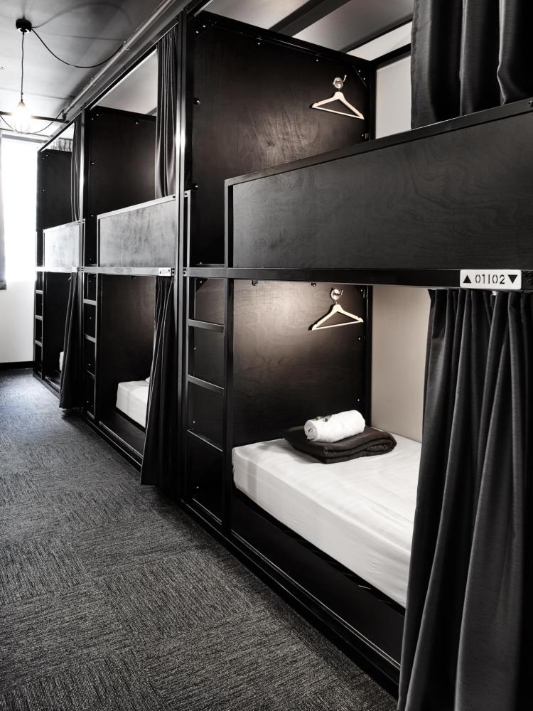 A row of capsule beds in a room with black walls create a modern atmosphere at The Pod Sydney.