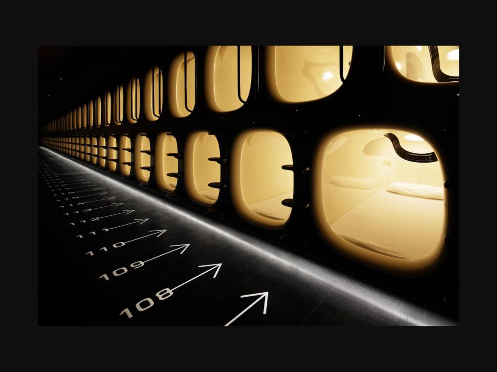 A long, well-lit hallway lined with numerous pods at 9h nine hours Narita Airport.