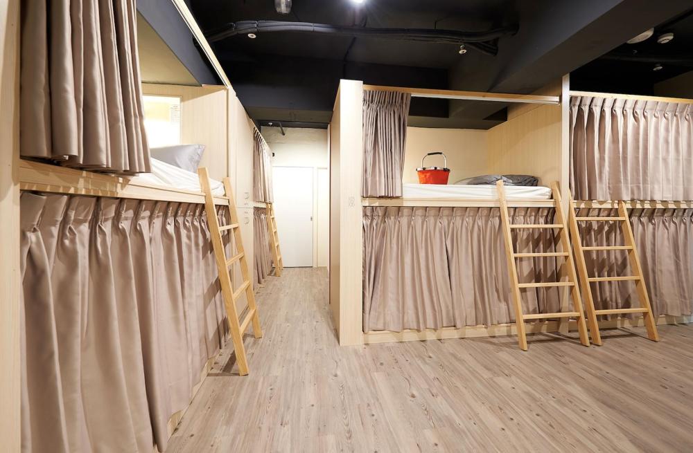 Several curtained pods feature in Ease Single Inn, Taiwan. There are wooden ladders to reach capsules on the top bunk.