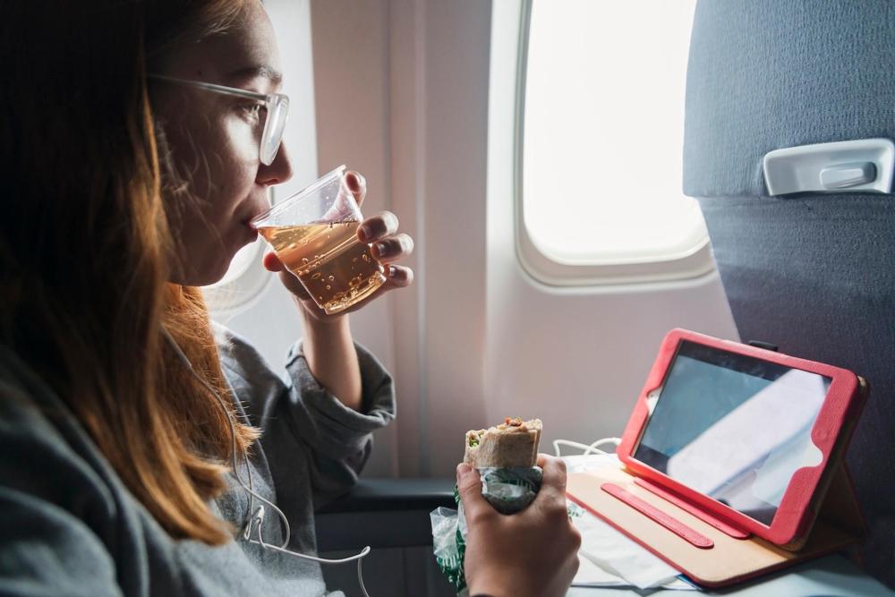 A girl sips a bubbly drink in a plastic cup on a plane, she has a wrap also