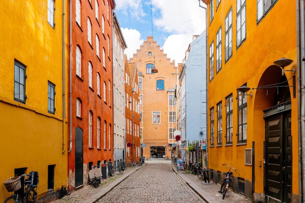 Orange and red buildings are depicted down a narrow street in Copenhagen