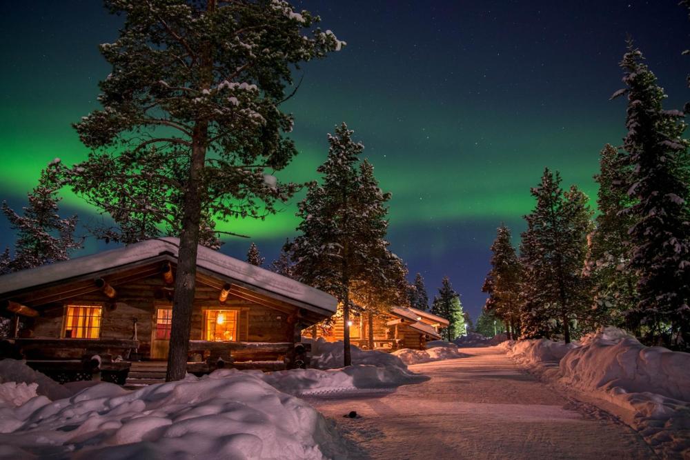 Eine Holzhütte im Vordergrund vervollkommnet die schillernden grünen Polarlichter im Hintergrund