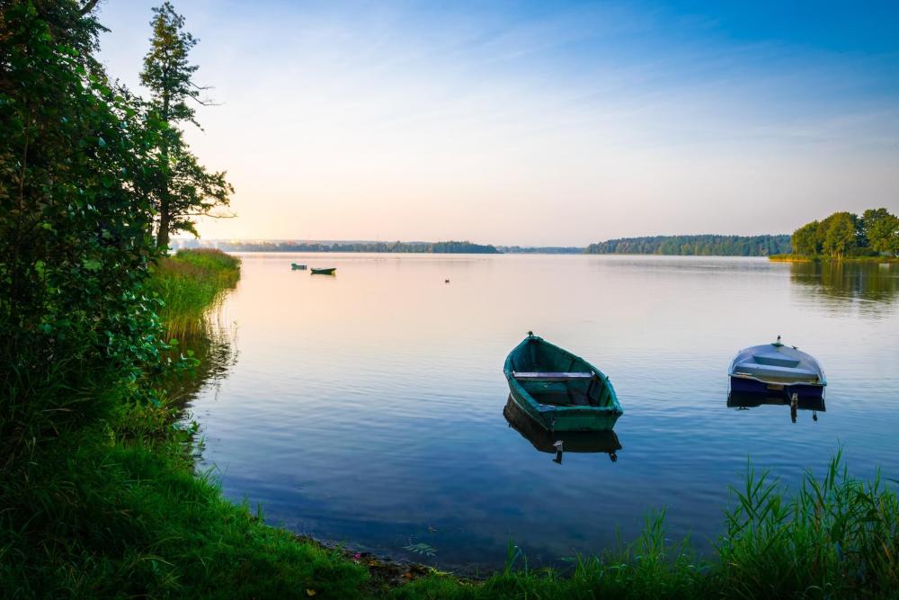 A few rowing bots on Ełk Lake featuring a sky with yellowish and pink hues in the background