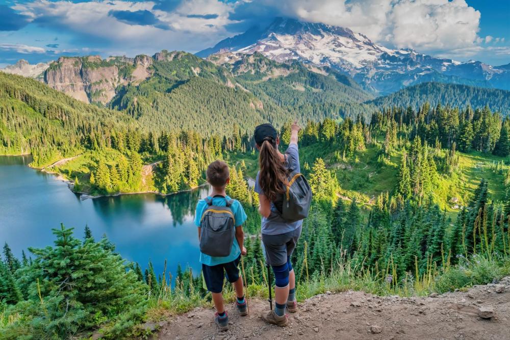 Two children stand on a trail, gazing at a lake and the majestic mountain range of Mount Rainier National Park.