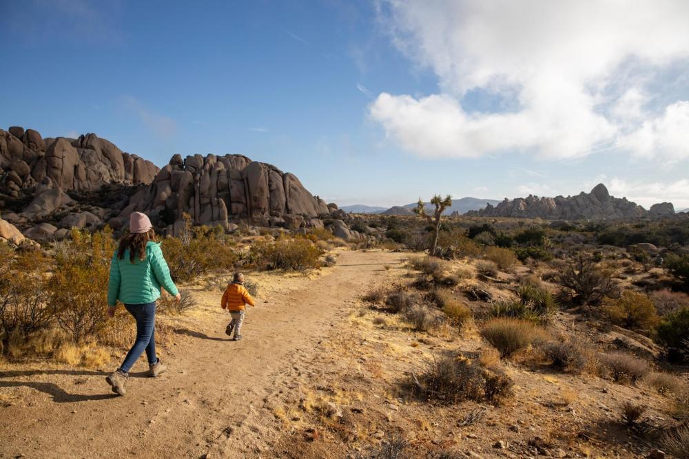 A woman and child walk on a desert trail in Palm Springs, with the vast desert landscape stretching out around them.