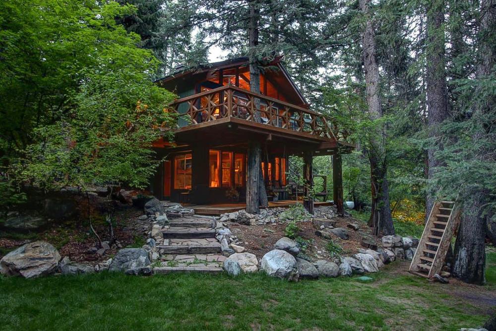 A tree house nestled in the woods of Utah, overlooking a serene stream, surrounded by lush greenery.