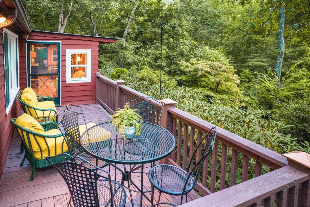 A deck with chairs and a table, providing a scenic overlook of the woods at The Treehouse in North Carolina.