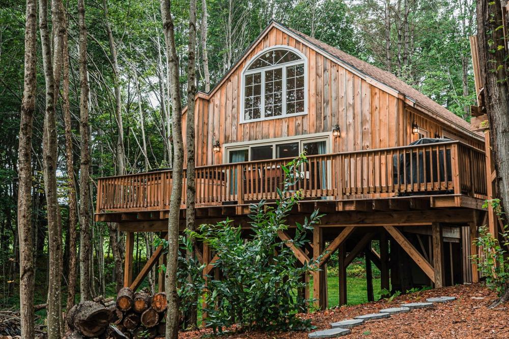 A picturesque house featuring a deck, situated on a hill, showcasing the tranquil beauty of Moonlight Treehouse, Maine.