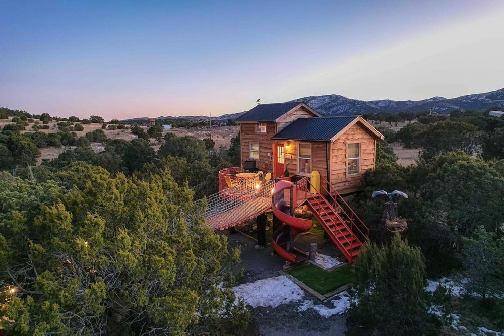 A tree house with a slide nestled in the woods of Crow's Nest, New Mexico, surrounded by lush greenery.