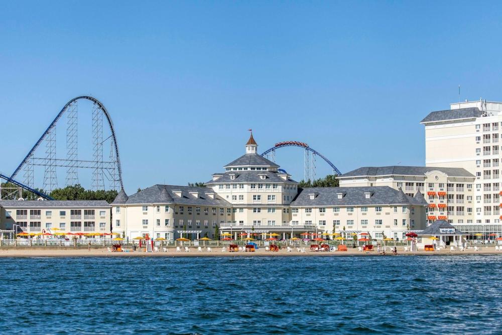 Cedar Point Hotel Breakers features as a large cream hotel. In the foreground, a roller coaster and a scenic beach view can be seen in Ohio.