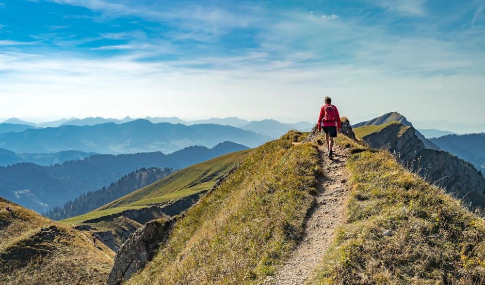 A person on a mountain peak gazes at the expansive valley below, with the beautiful backdrop of Munich in the distance.