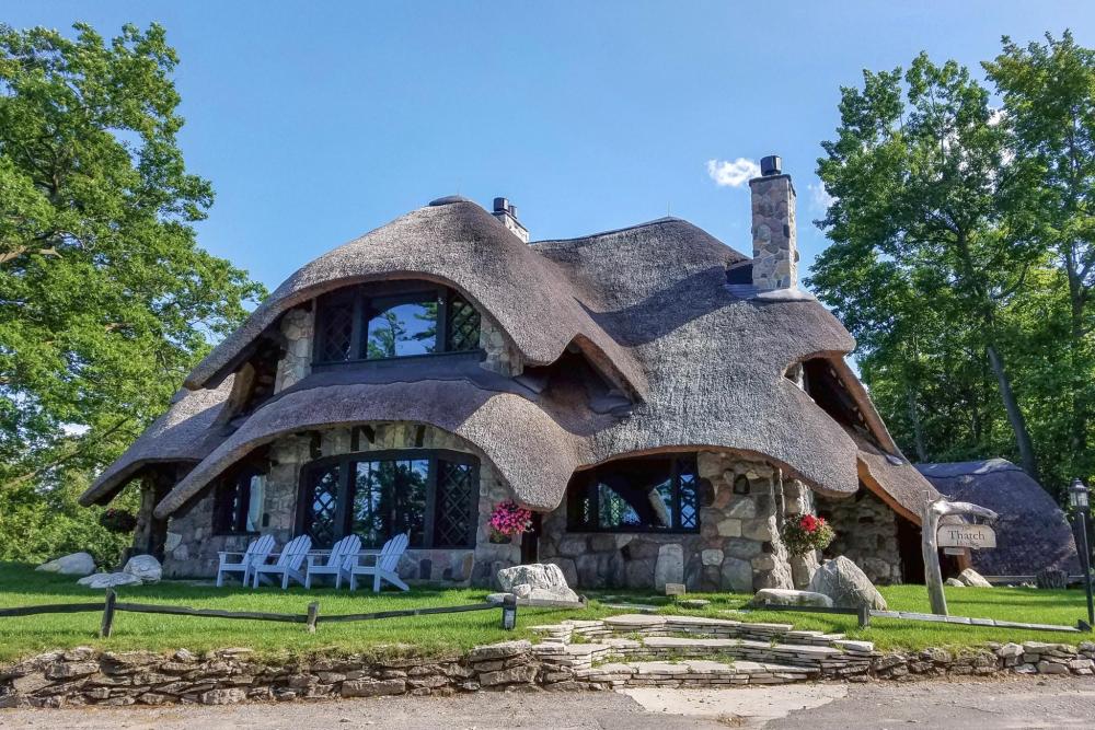 A picturesque thatched house surrounded by a stone path and a vibrant lawn in Charlevoix, Michigan.