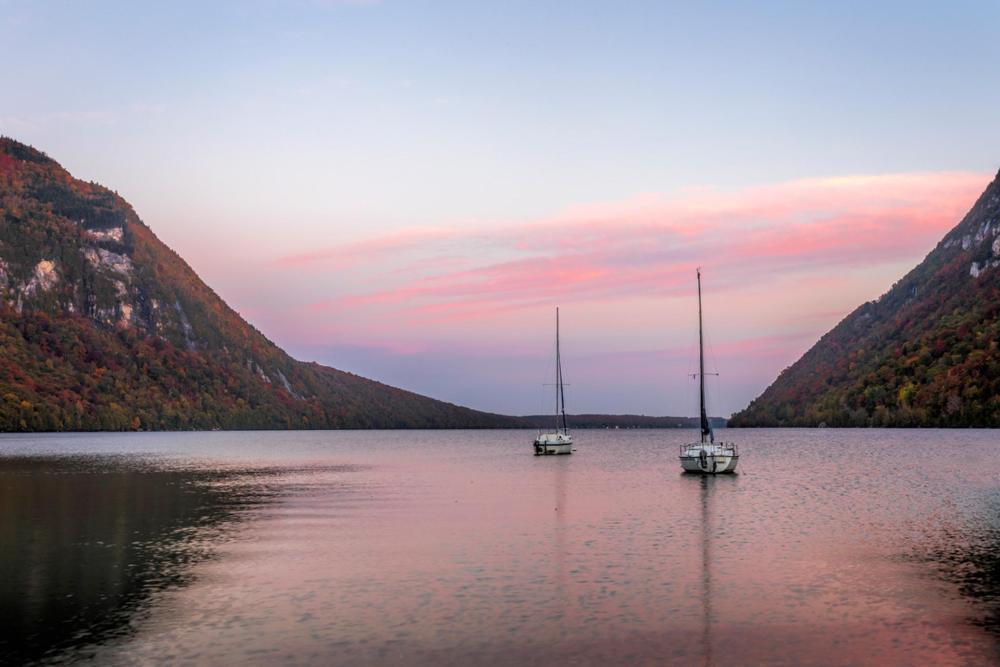 Two sailboats glide on Lake Willoughby, Vermont, surrounded by majestic mountains in the background.