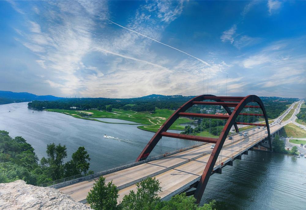 A bridge over Lake Austin, Texas, spanning a serene river with a clear sky in the background.
