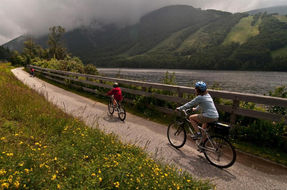 Two cyclists ride along a scenic path beside Echo Lake in New Hampshire, surrounded by nature's beauty.