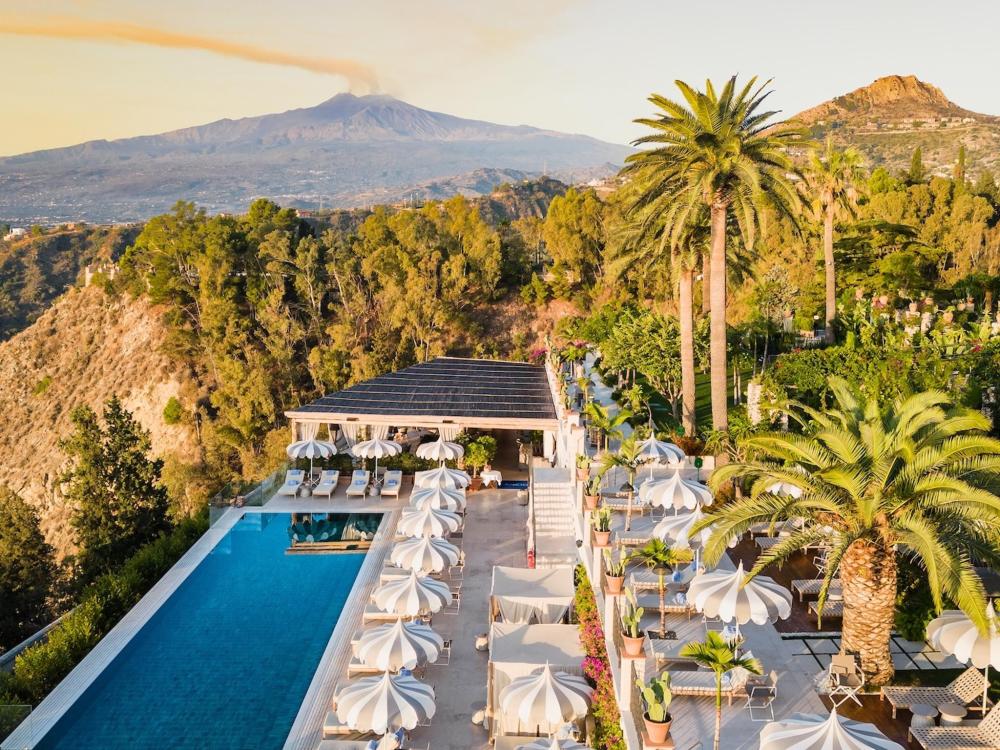 The San Domenico Palace hotel is highlighted by a refreshing pool and palm trees in a picturesque setting.