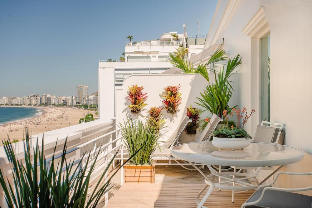 A balcony at the Copacabana Palace Hotel features a table and chairs with a stunning view of the beach below.