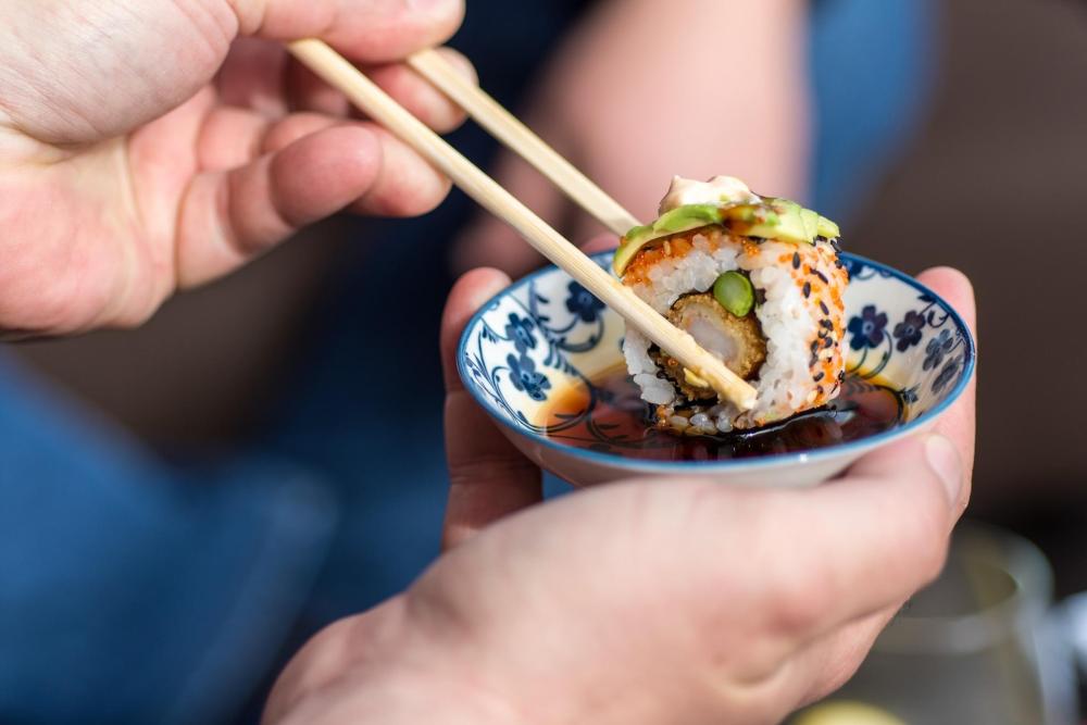 Hand holding chopsticks to dip sushi roll in soy sauce