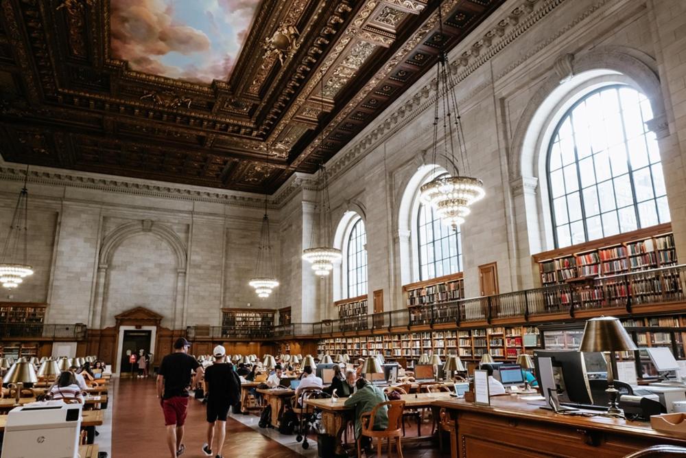 People studying, working and reading inside the New York Public Library, surrounded by books and elegant architecture