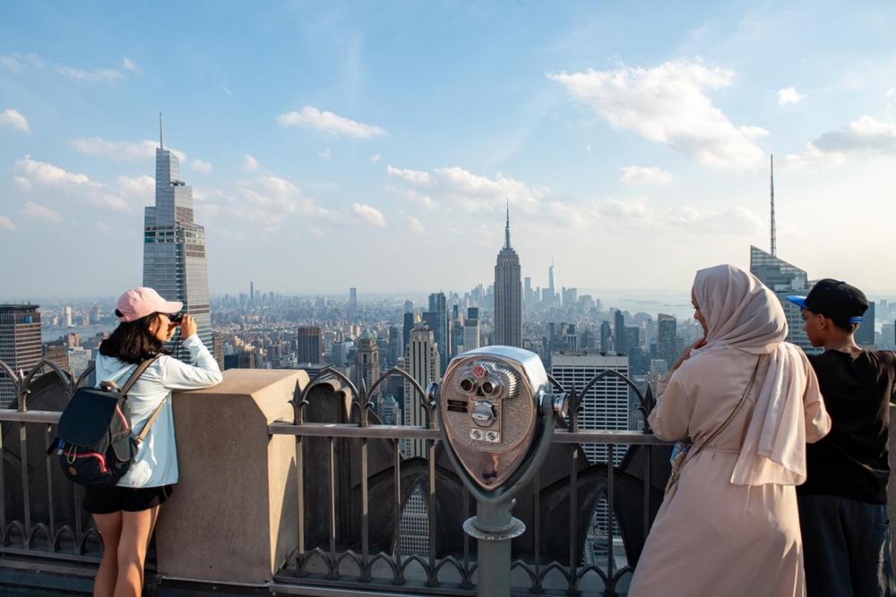 Three people gaze at the city skyline from the observation deck of 'Top of the Rock'