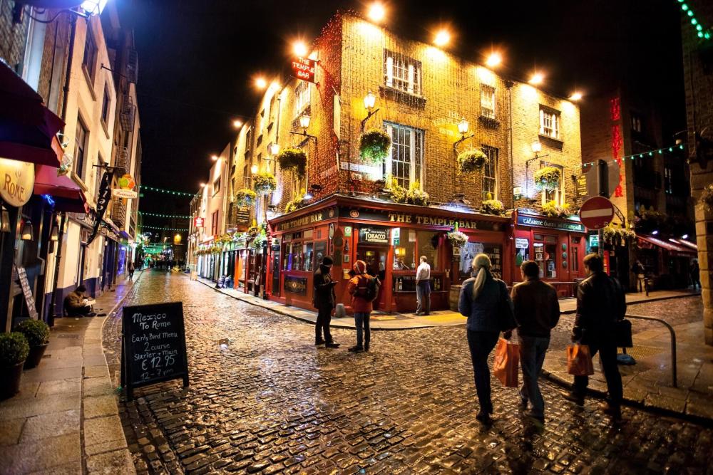 People stroll along a cobblestone street outside of Temple Bar, Dublin, illuminated by soft lights on a serene night