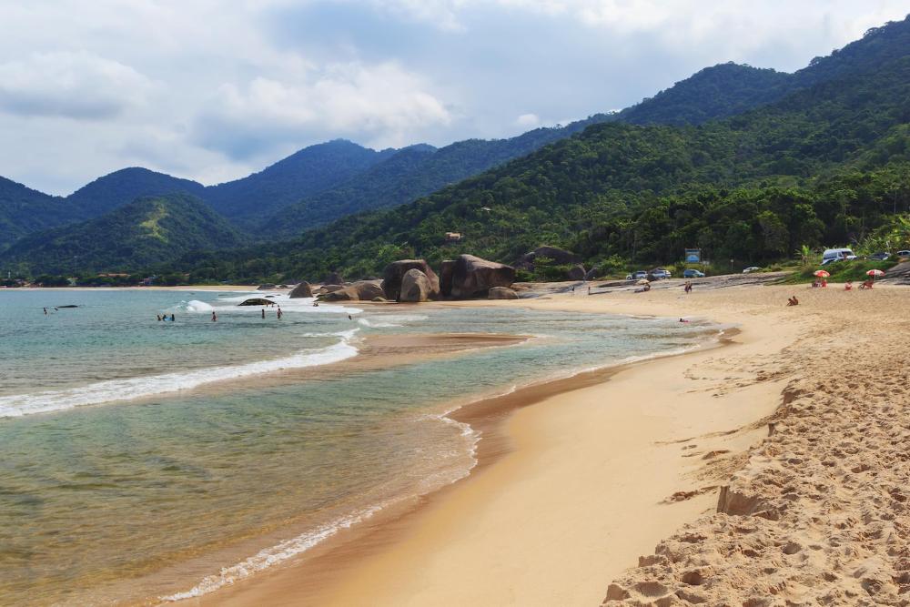 A sandy beach in Paraty, with gentle waves lapping at the shore under a clear blue sky